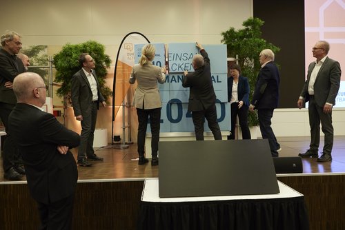 Auf der Bühne wird von mehreren Personen ein großes neunteiliges Puzzle aus Würfeln zusammengebaut. 