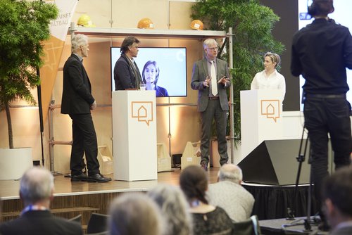 Diskussionsrunde auf der Bühne mit von links nach rechts: Frank Hettler, Udo Engelhardt, auf dem Bildschirm zugeschalten Uta Weiß, Carel Mohn und Janine Steeger.