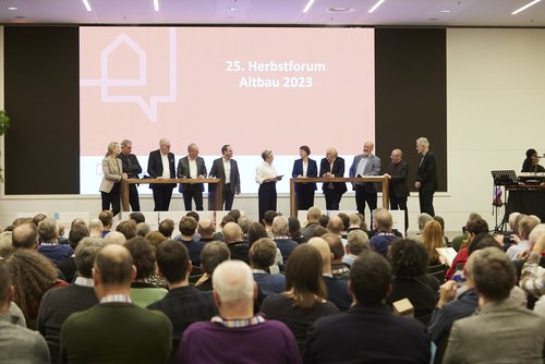 Diskussionsrunde auf der Bühne an zwei großen Tischen mit elf Personen. 