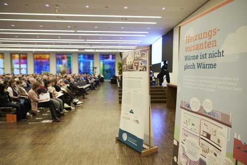 Seitlicher Blick ins Saalpublikum, rechts daneben sind einige Info-Aufsteller von Zukunft Altbau zu sehen. 