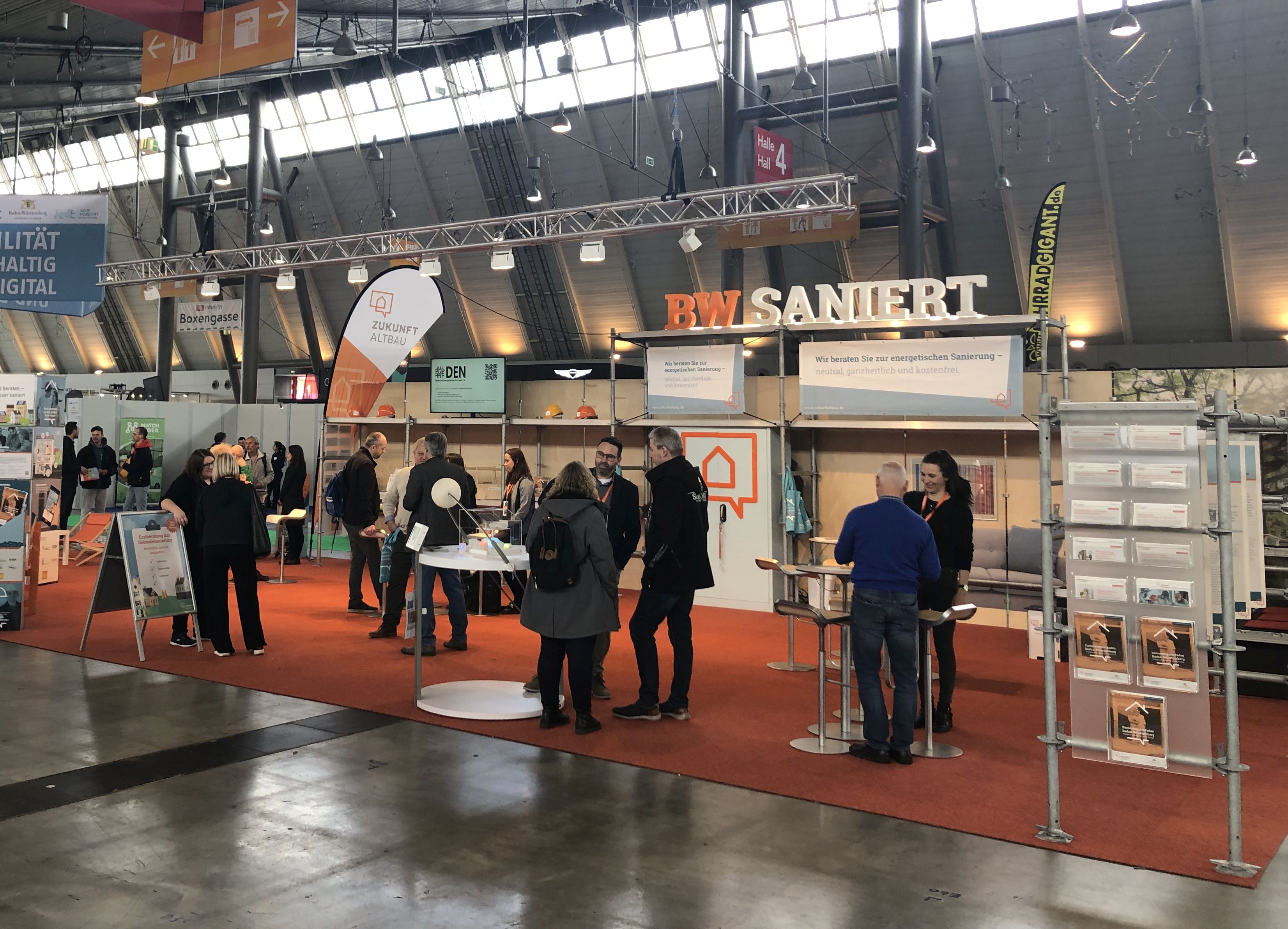 Veranstaltung mit Wanderausstellung. Zu sehen sind verschiedene Stände und mehrere Personengruppen, die sich austauschen.