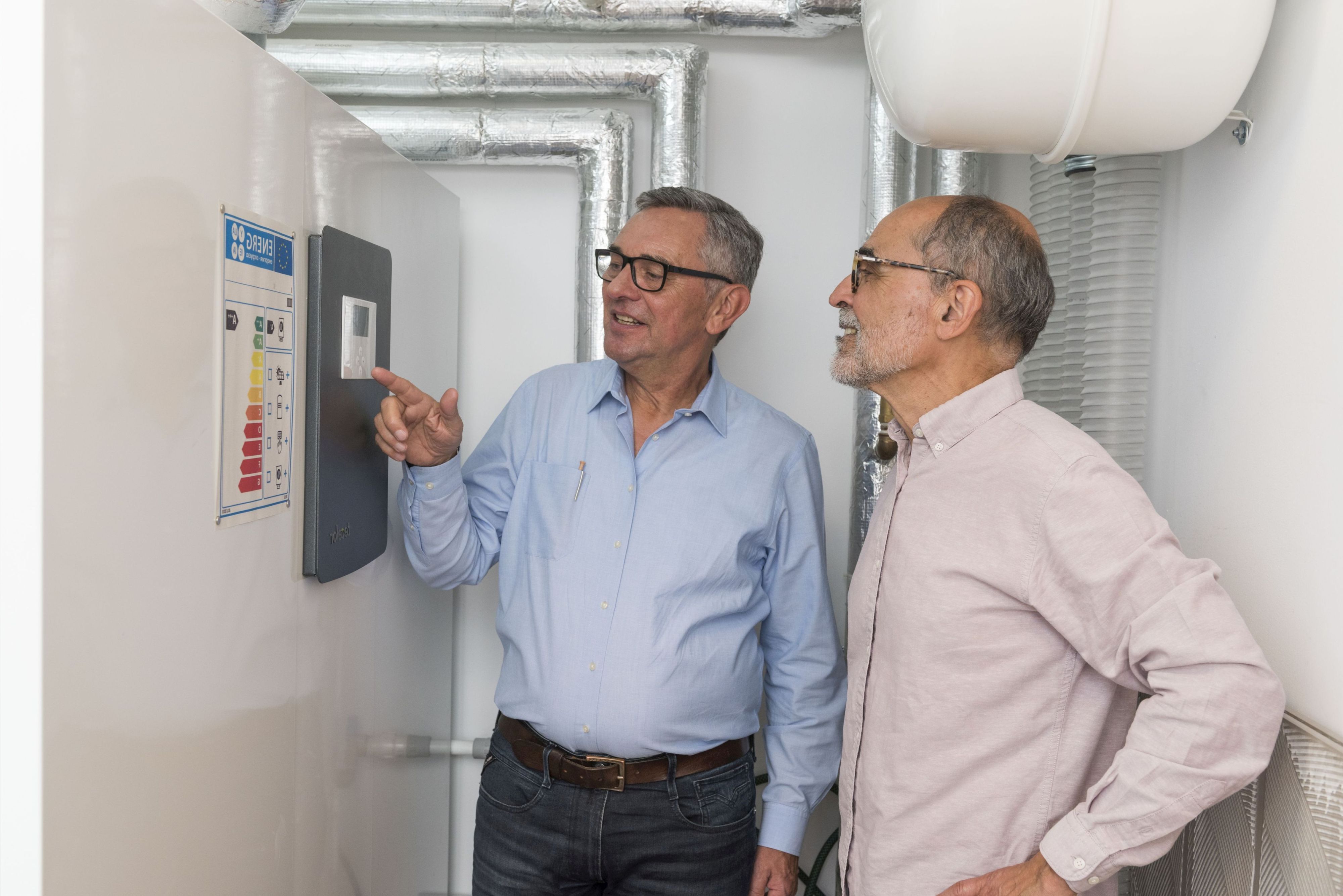 Ein Energieberater steht gemeinsam mit einem Hauseigentümer im Heizungsraum. Der Energieberater zeigt auf das Display.